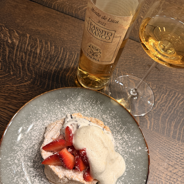 An alternate close-up angle of the Vaona Passito Bianco bottle and poured glass, beautifully capturing the golden color of the wine alongside the vibrant red strawberry dessert.