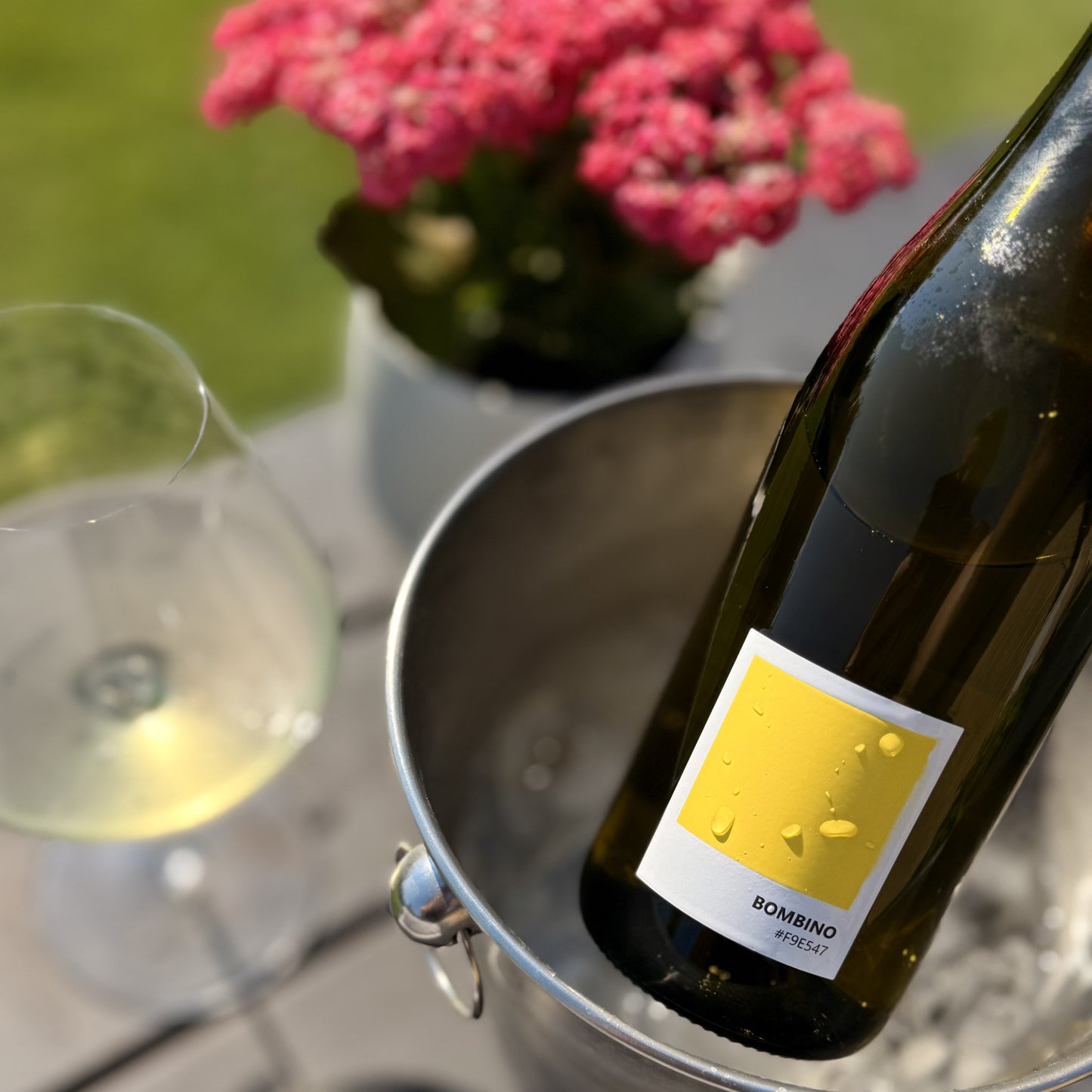 Bottle of Bombino wine in a bucket with a glass of wine and pink flowers in the background.