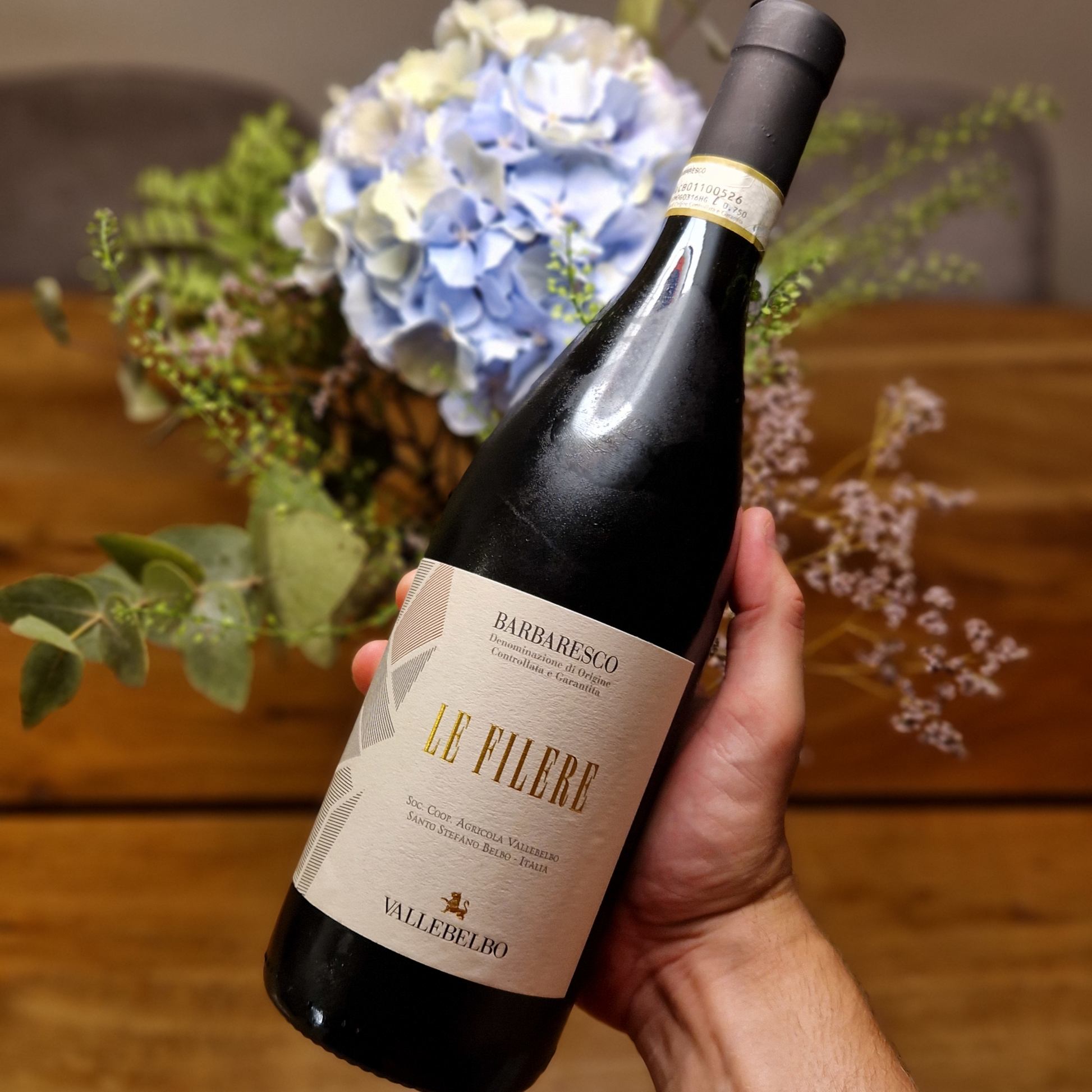 Bottle of Le Filere Barbaresco wine held by a hand with flowers in the background