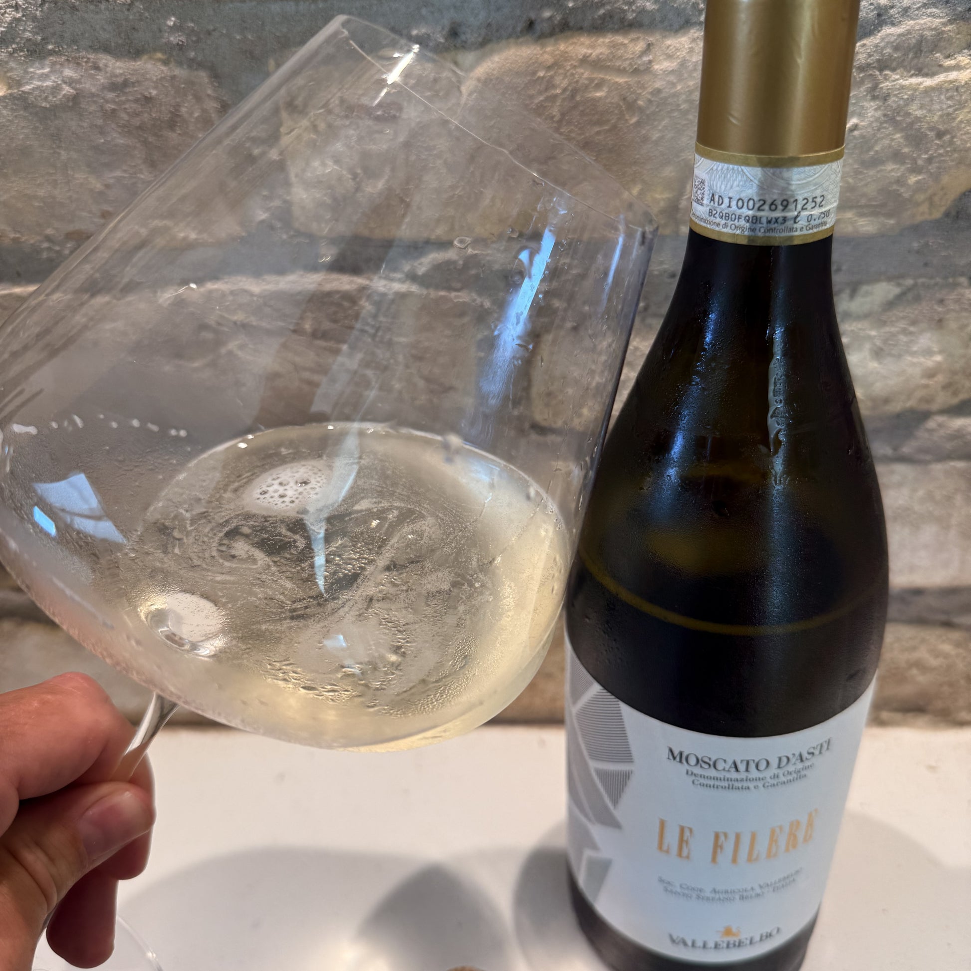 Bottle of Moscato d'Asti Le Filere with a glass of wine against a stone wall background