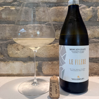 Bottle of Le Filere Vallebelbo Moscato d'Asti wine with a glass and cork on a stone surface.
