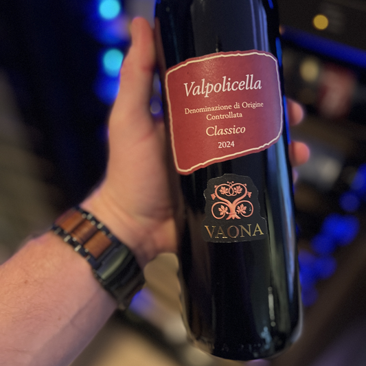 A close-up shot of a man confidently holding a bottle of Vaona Valpolicella Classico DOC, framing it to clearly highlight the artistic and clean details of the front label.